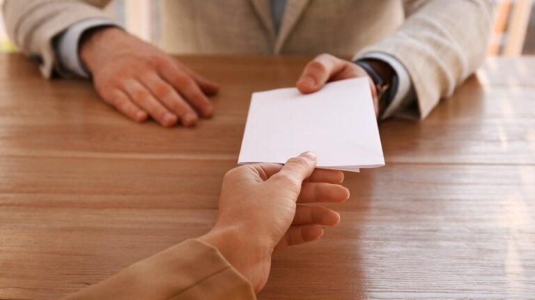 Foto de primerísimo plano de un papel plegado pasando de una mano a otra, de una persona a otra; haciendo referencia a las cartas de presentación.
