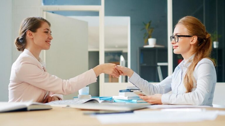 Fotos de dos mujeres en una ofician de empleo dándose la mano en señal de acuerdo sobre ayudas y prestaciones a través de Lanbide.