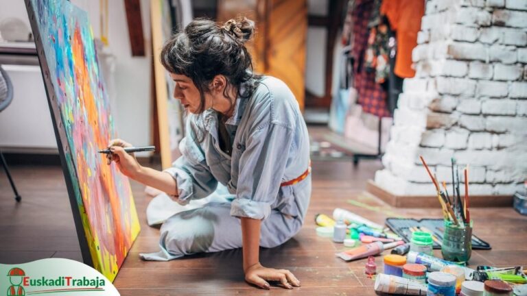 Foto de una mujer pintando un cuadro sentada en el suelo en referencia a las ofertas de empleo de Lanbide sobre información y manifestaciones artísticas.