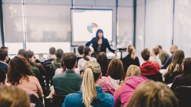 Foto de una profesora dando una clase de formación a un grupo amplio de trabajadores y trabajadoras.