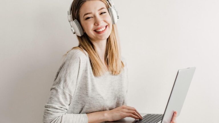 Foto de una mujer joven con auriculares y un portátil en las manos.