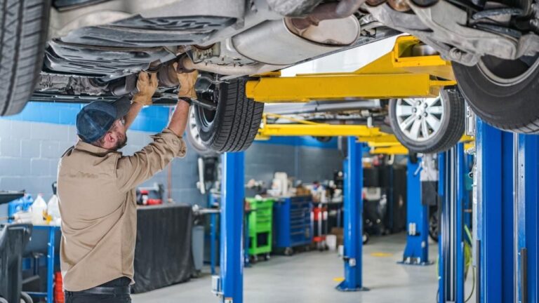 Foto de un taller de mecánica reparando un vehículo que está elevado.